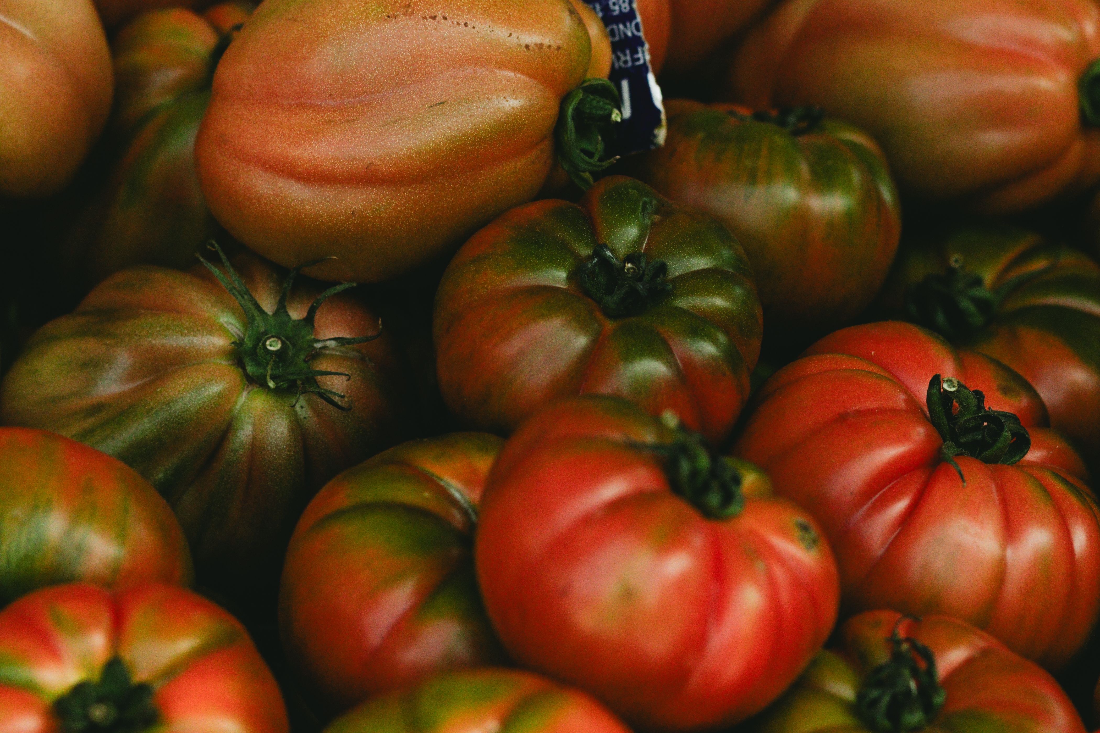 A vibrant collection of heirloom tomatoes in a wicker basket on soil. Perfect for organic and healthy eating themes.