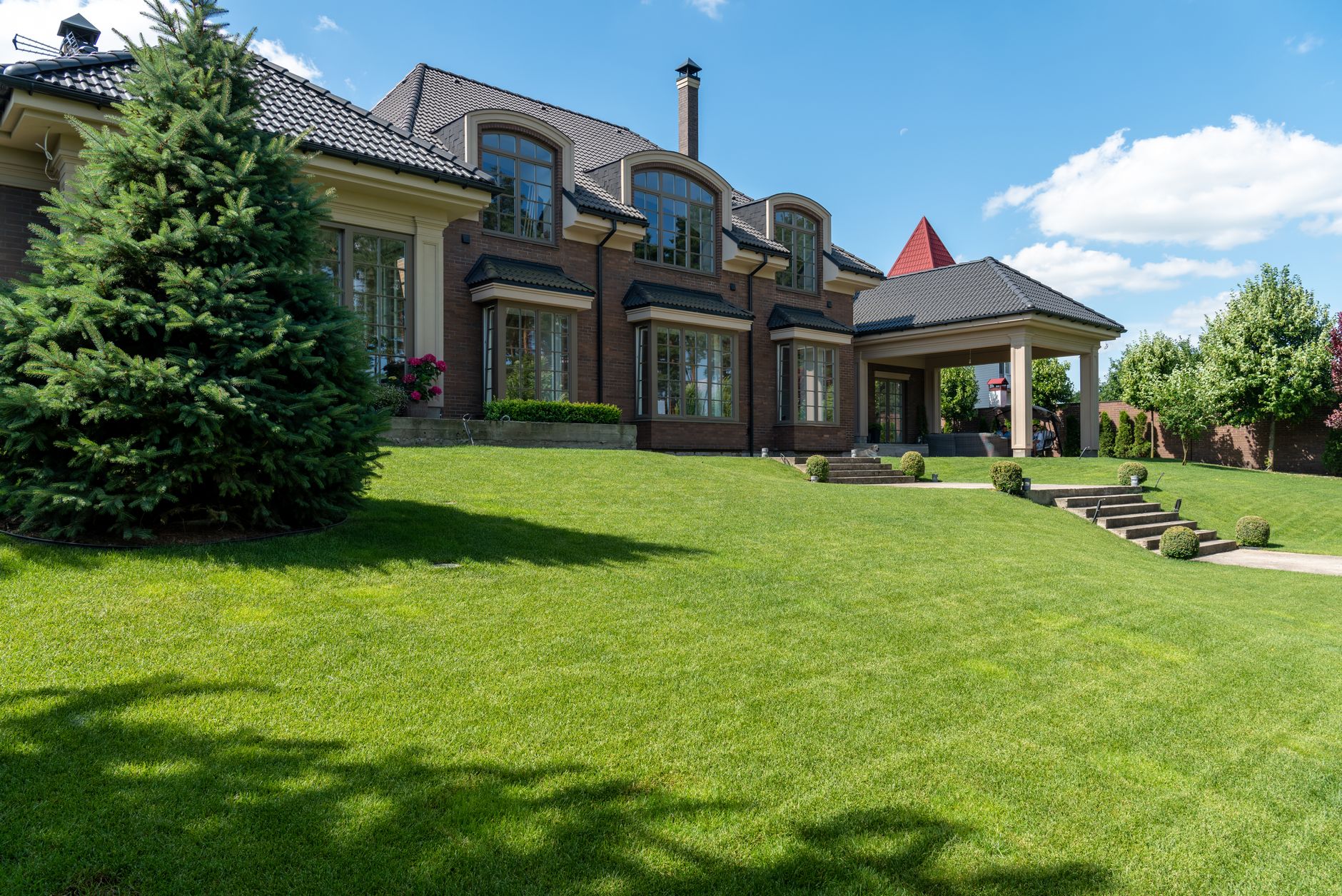 A green lawn being watered by a sprinkler on a sunny summer day, showing proper irrigation technique for keeping grass healthy during hot weather